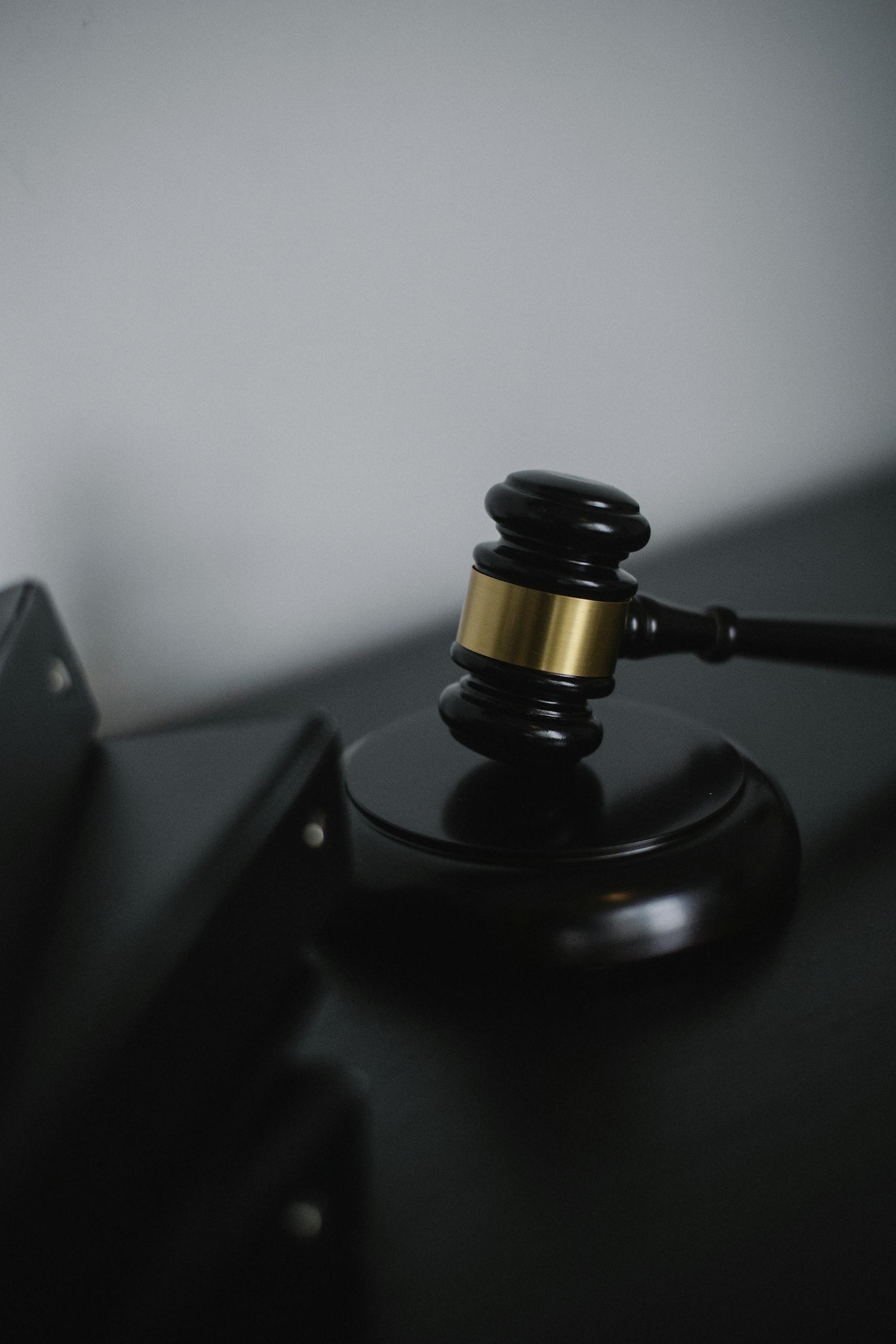 Black wooden gavel with golden strip on table near stack of folders in courthouse